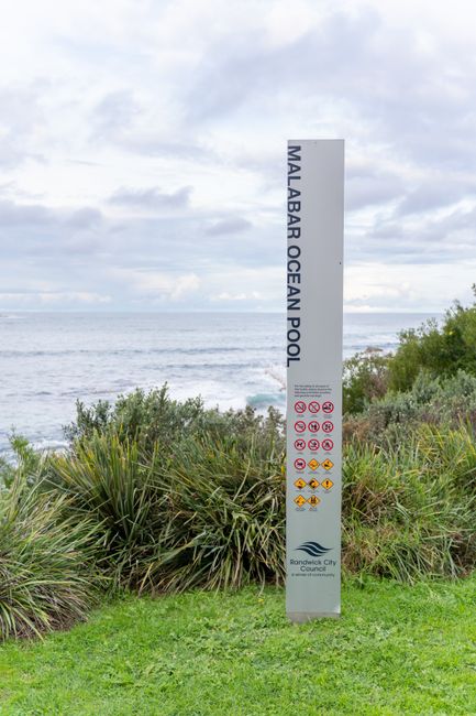 Two red Cheltenham Borough Council alcohol-free zone signs attached to a black metal pole outdoors. The signs display white text indicating that drinking alcohol within the zone is prohibited and that